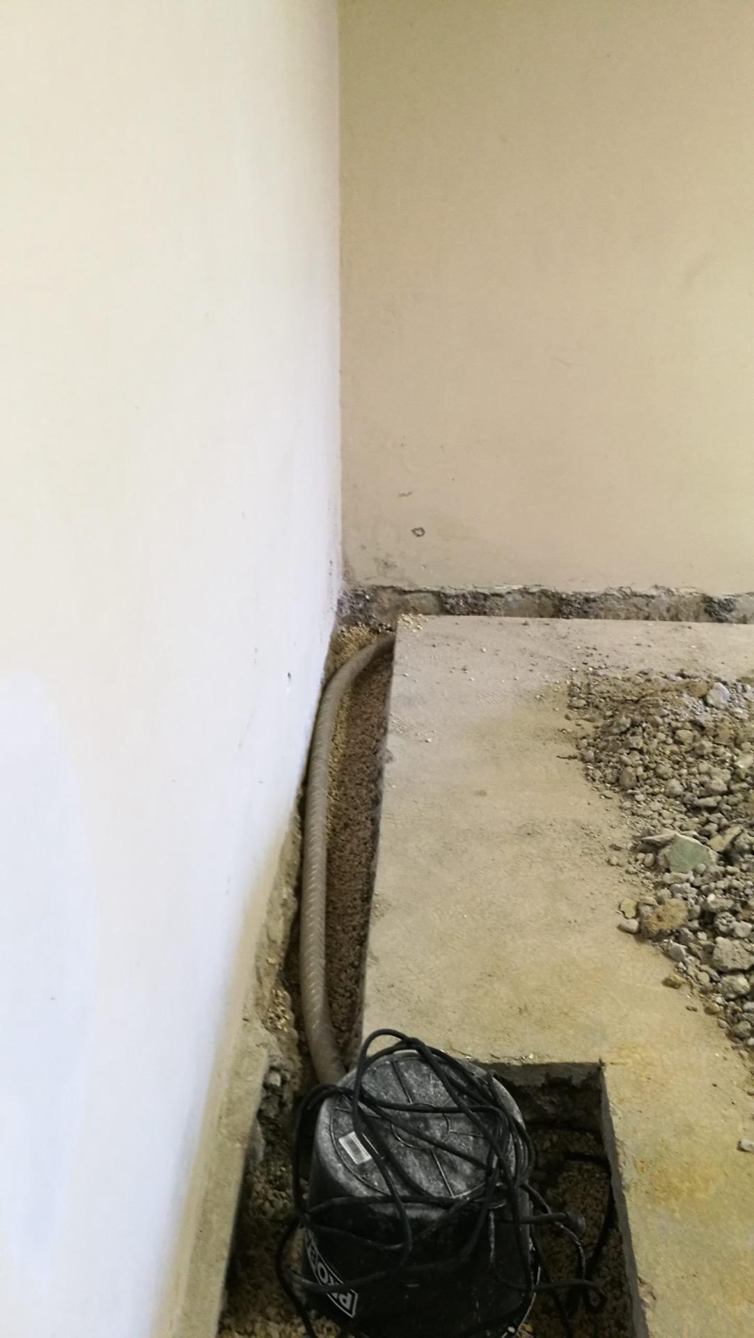 Helyiség sarkában kaviccsal feltöltött árok gégecsővel, a padlóba vágott aknában fekete búvárszivattyú.